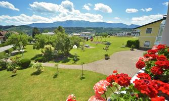 An idyllic garden landscape with blooming flowers and a playground. In the background, gentle mountains and a blue sky can be seen.