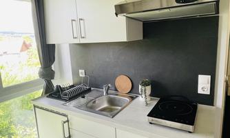 A modern kitchen with white cabinets and a black countertop. Above the sink hangs a range hood, and a window provides plenty of daylight.