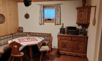 A cozy dining area with a wooden table and a padded bench. Against the wall is a traditional wooden cabinet and a window with curtains.