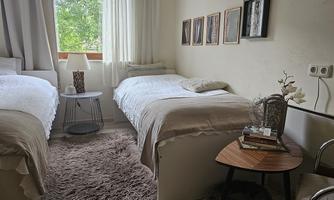 A cozy bedroom with two single beds and a small table. Large windows provide plenty of daylight and a pleasant atmosphere.