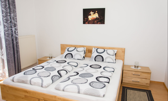 A modern bedroom with a double bed and neutral colors. The walls are white, and there is decorative wall art above the bed.