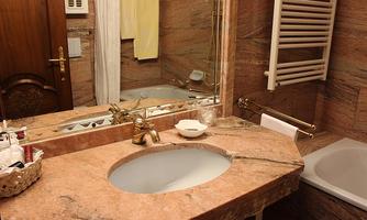 An elegant bathroom with a marble sink top and a large mirror. In the background, a bathtub and towels are visible.