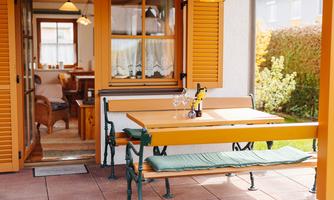 An inviting outdoor area with a table and benches in a cozy ambiance. The orange shutters and the view of the greenery create a pleasant atmosphere.