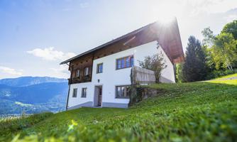 A beautiful house on a meadow with a view of the mountains. The sun is shining brightly and the sky is clear.