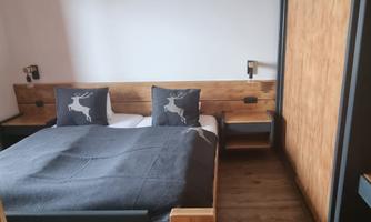 A cozy bedroom with a large bed and rustic wooden furniture. The walls are light, and the pillows feature a deer motif.