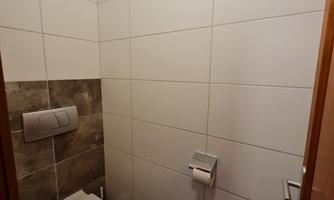 A small bathroom with modern tiles. There is a toilet and a towel holder on the wall.