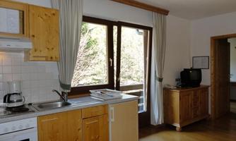 A bright wooden kitchen with a window that offers a view of the outdoors. The furnishings are simple and functional with a stove, sink, and kitchen cabinets.
