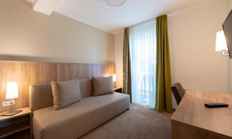 A modern hotel room with a cozy couch and desk. Large windows provide bright light and an inviting atmosphere.