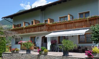 A charming house with a wooden balcony and blooming plants. The outdoor area is inviting with seating and sun protection.