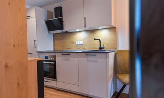 A modern kitchen with bright cabinets and an elegant countertop. The warm wooden cladding and the simple decor create a cozy atmosphere.