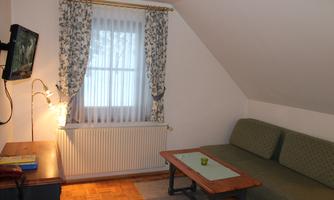 A cozy room with a sofa and a wooden table. A window with curtains lets in a lot of light.