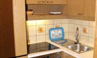 A small kitchen with wooden furniture and a bright tile backsplash. It is equipped with a stove, sink, and refrigerator.