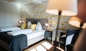 A stylish room with a large bed and decorative pillows. The walls are adorned with an elegant pattern, and a desk with a chair is present.