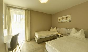 A bright room with two beds and a modern table. Large windows provide plenty of natural light and a view outside.