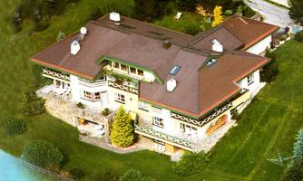 A large, elegant house surrounded by a green garden. The roof has a distinctive architecture and there are several windows that let in plenty of light.