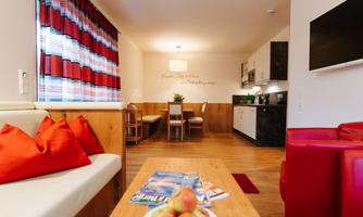 A cozy living room with a modern kitchen. Red cushions and a table with fresh apples create an inviting atmosphere.