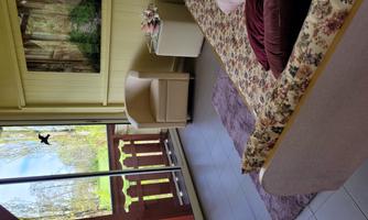 A cozy room with a flower-patterned sofa, an armchair, and large windows overlooking a green meadow. The room is bright and invitingly designed.
