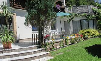 A beautiful garden with colorful flowers and a well-manicured lawn.  
Next to the terrace stands a sun umbrella and tall plants create a pleasant atmosphere.