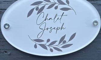 An oval sign with the inscription "Chalet Joseph" and decorative branches. The sign is fixed to a wooden background.