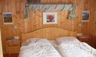 A cozy bedroom with wood paneling and two beds. Pictures hang on the walls, and there are nightstands with lamps.
