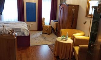 Room with double bed, wooden wardrobe, desk, seating area with two armchairs and round table, tea station and infrared heater on the wall.