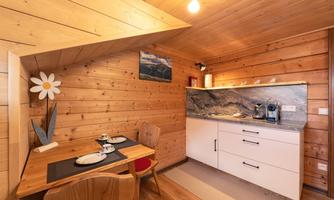 A cozy kitchen with wooden walls and modern furniture. A small dining table is decorated with dishes and cutlery.