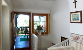 A bright hallway with a staircase and wood details. A small balcony is visible through the window.