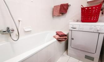 A bathroom with a bathtub and a washing machine. The walls are light and there are towels in various shades of red.