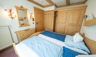 A bright bedroom with two single beds and traditional wooden interior. On the wall, there is a mirror and a wardrobe.