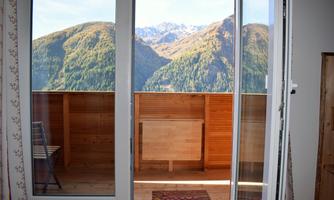 A balcony with a view of high mountains and a clear sky. The wooden cladding gives the room a warm atmosphere.
