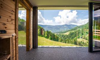 A modern room with large windows and a view of green mountains and a clear sky. The natural surroundings create a relaxing atmosphere.