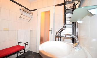 A modern bathroom with white tiles and a large sink. There is a red seating area and a towel holder on the wall.