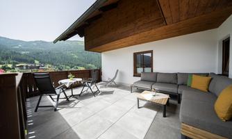 A modern terrace with a cozy seating area and a view of green hills. The space is bright and inviting, perfect for relaxing outdoors.