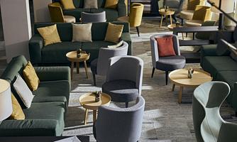 A modern lounge area with elegant sofas and comfortable chairs. There are several small tables and a bright, inviting atmosphere.