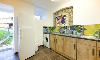A modern kitchen with wooden cabinets and white appliances. On the wall is a creative mural and the floors are tiled.