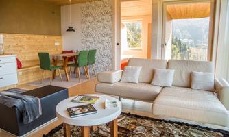 A modern living room with a comfortable sofa and a small table. The room has large windows with a view of the landscape.
