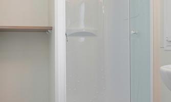 A modern shower niche with white walls and a glass door. The floor is made of wood and there is a space for toiletries.
