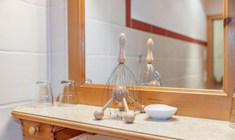 A clean kitchenette with a mirror, a whisk, and two glasses. A small white bowl is also on the countertop.