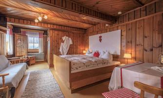 A cozy room with wooden walls and a large double bed. The room features a sitting area and atmospheric lighting.