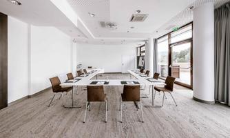 A modern meeting room with clean lines and plenty of natural light. The room is equipped with a large table and several chairs.
