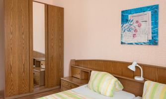 A simple bedroom with a wooden bed and colorful striped bedding. A picture hangs on the wall, and next to it stands a wardrobe with a mirror.