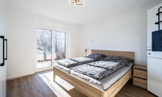 A modern bedroom with a double bed and two mattresses.  
Large windows let in plenty of daylight and offer a view outside.