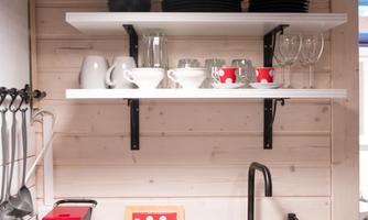 A modern kitchen unit with a red coffee machine and a stylish sink. Above the countertop, shelves with dishes and glasses hang.