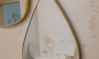An elegant water droplet mirror hangs on the wall. In the mirror, a white cabinet and decorative elements are visible.