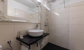 A modern bathroom with an elegant washbasin and a large mirror. The walls are bright, and the furnishings are stylish and functional.