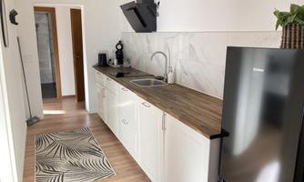 A modern kitchen with a wooden countertop and white cabinets. In the background, a refrigerator and a carpet are visible.