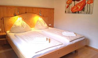 A cozy bedroom with a double bed and two pillows. A picture of red flowers hangs on the wall.