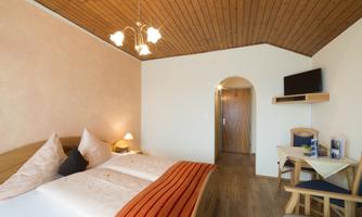A cozy bedroom with two beds and modern furniture. The wooden ceiling and natural light give the room a warm atmosphere.