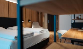 A modern hotel room with a large double bed and wooden paneling. There is a chair on the table and the lighting is soft.