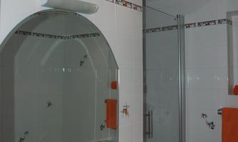 A modern bathroom with a sink, mirror, and a glass shower. Orange towels and a colored tile border complement the decor.